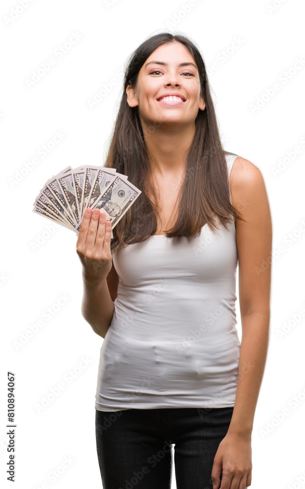 Young hispanic woman holding dollars with a happy face standing and smiling with a confident smile showing teeth Young hispanic woman holding dollars with a happy face standing and smiling with a confident smile showing teeth