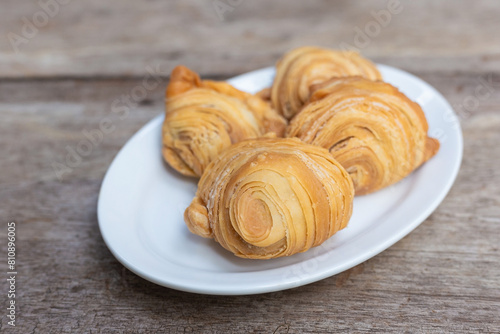 Curry puffs are a snack of Central in Thailand. It is a small pie that contains chicken and potatoes in a deep fried pastry shel่l in a white plate on a wooden table.