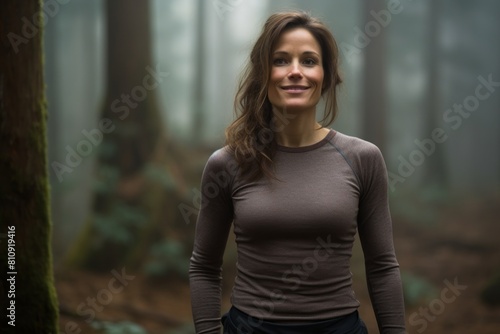 Portrait of a satisfied woman in her 30s sporting a long-sleeved thermal undershirt isolated on backdrop of a mystical forest