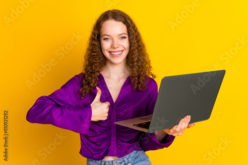Photo portrait of lovely young lady hold netbook thumb up dressed stylish violet garment isolated on yellow color background photo