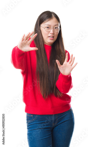 Young Chinese woman over isolated background wearing glasses afraid and terrified with fear expression stop gesture with hands, shouting in shock. Panic concept.