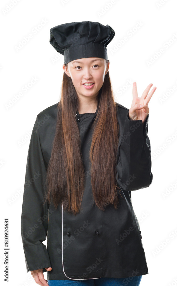 Young Chinese woman over isolated background wearing chef uniform showing and pointing up with fingers number three while smiling confident and happy. Young Chinese woman over isolated background wearing chef uniform showing and pointing up with fingers number three while smiling confident and happy.