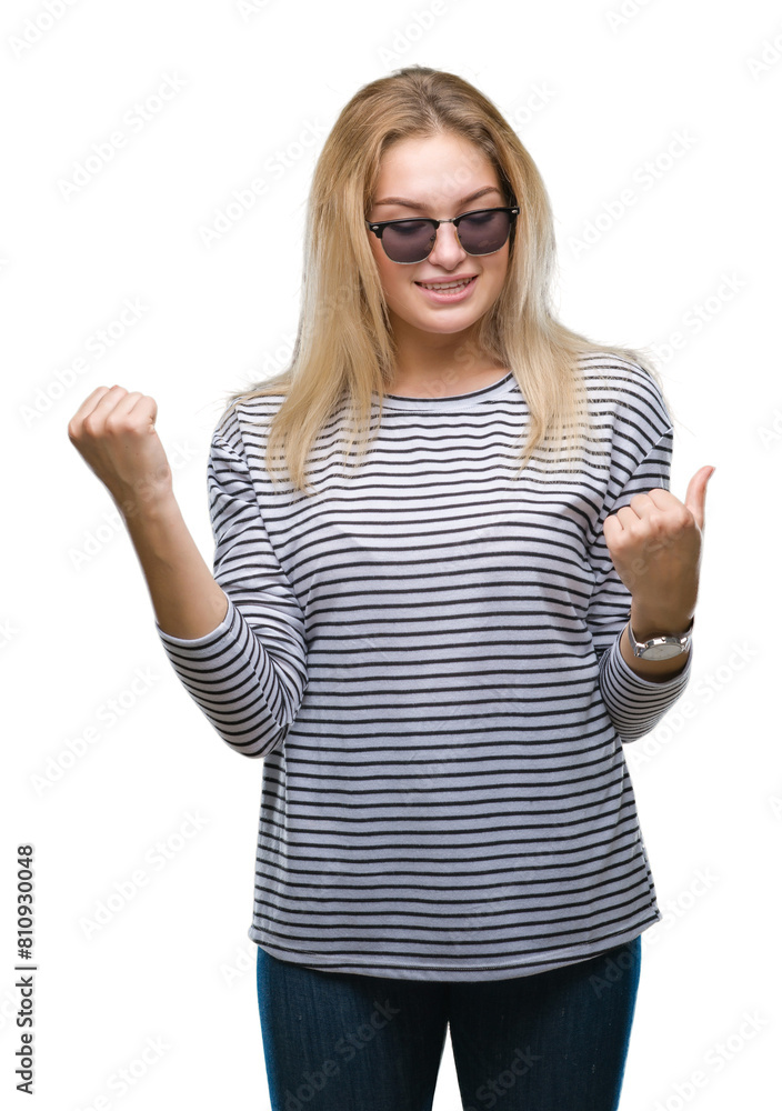 Young caucasian woman wearing sunglasses over isolated background very happy and excited doing winner gesture with arms raised, smiling and screaming for success. Celebration concept. Young caucasian woman wearing sunglasses over isolated background very happy and excited doing winner gesture with arms raised, smiling and screaming for success. Celebration concept.