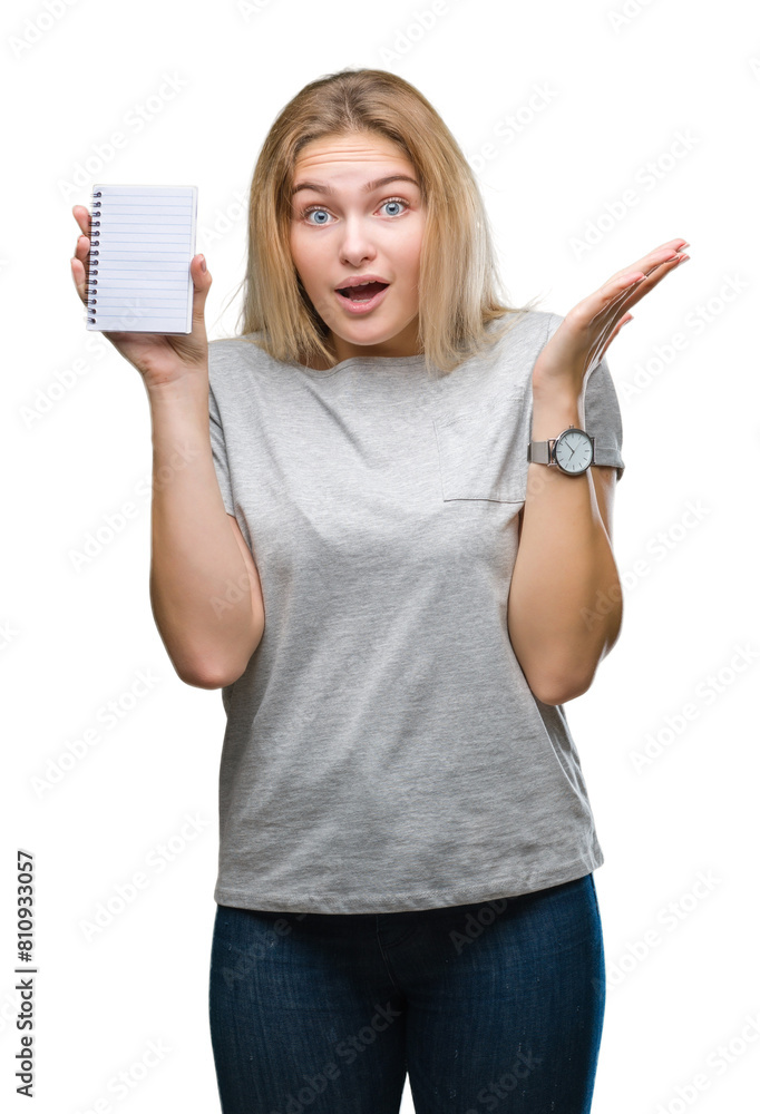 Obraz premium Young caucasian woman holding blank notebook over isolated background very happy and excited, winner expression celebrating victory screaming with big smile and raised hands