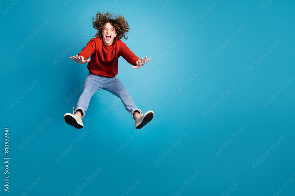 Full length photo of cheerful positive guy dressed red pullover jumping high emtpy space isolated blue color background