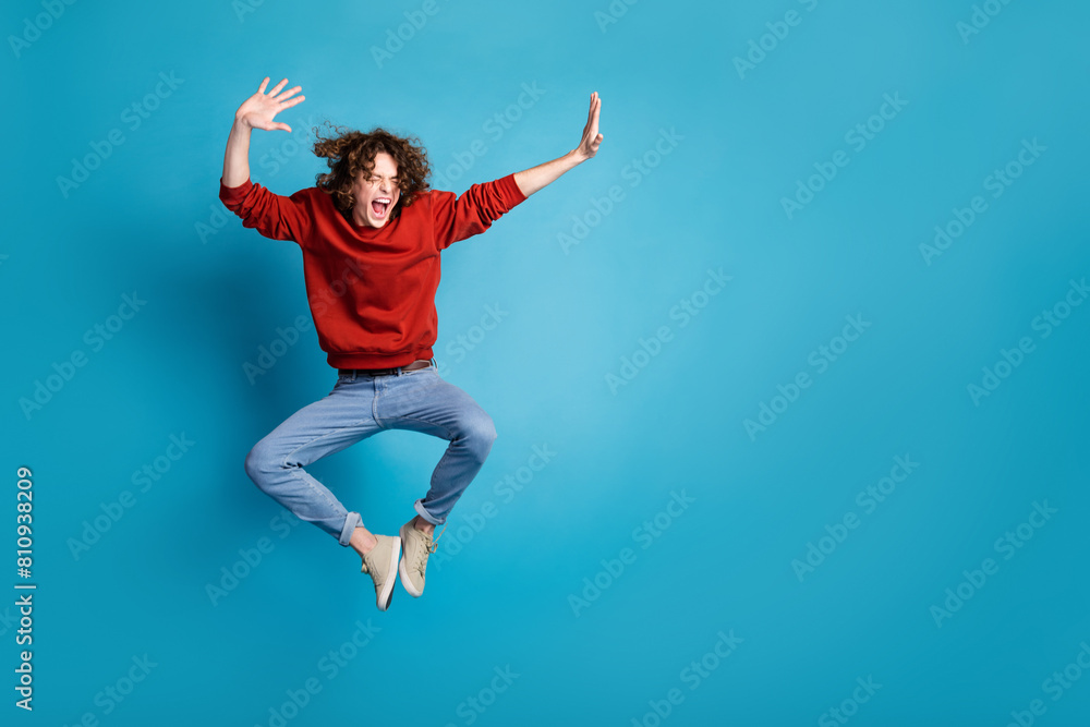 Full length photo of carefree positive guy dressed red pullover jumping high emtpy space isolated blue color background