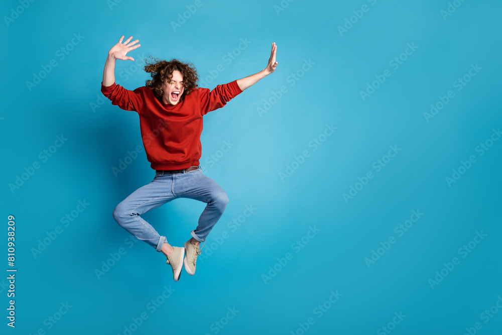 Full length photo of carefree positive guy dressed red pullover jumping high emtpy space isolated blue color background Full length photo of carefree positive guy dressed red pullover jumping high emtpy space isolated blue color background