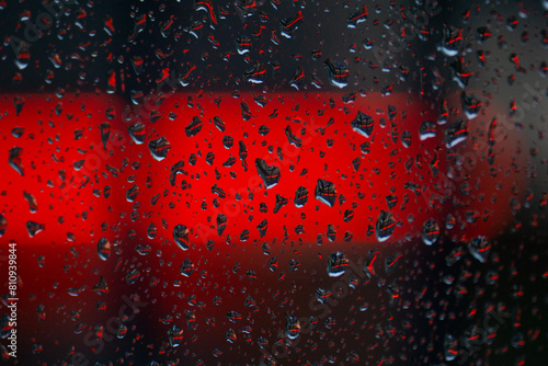 gocce di pioggia sul vetro di una finestra e sullo sfondo un neon rosso di un'insegna di un bar, sfocata
