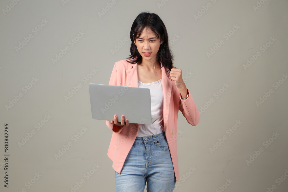 angry upset mad asian woman wearing formal casual outfit holding laptop computer on isolated background. angry upset mad asian woman wearing formal casual outfit holding laptop computer on isolated background.