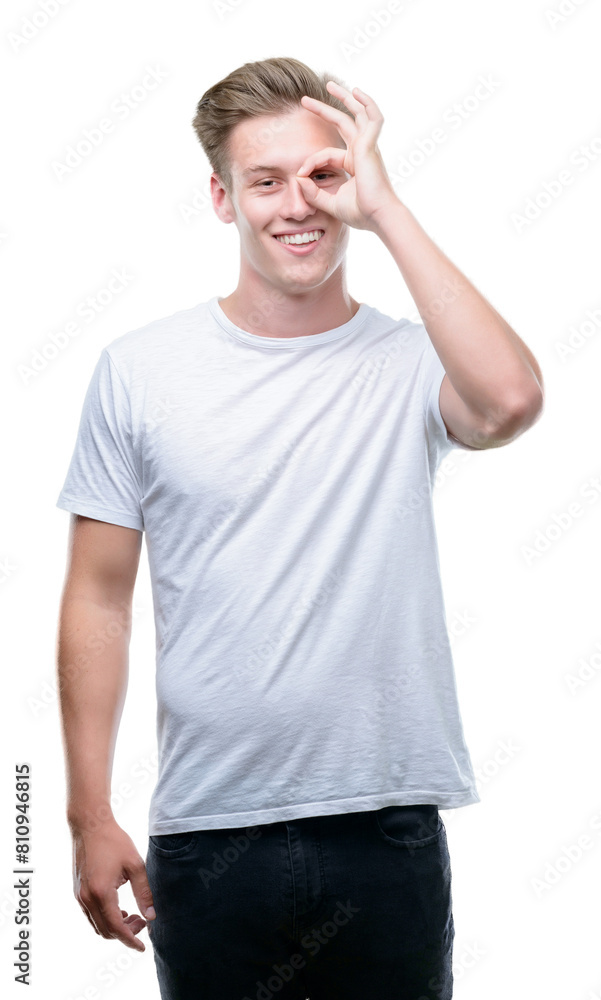 Young handsome blond man with happy face smiling doing ok sign with hand on eye looking through fingers Young handsome blond man with happy face smiling doing ok sign with hand on eye looking through fingers