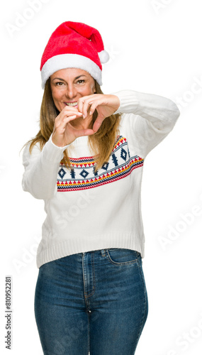 Middle age adult woman wearing winter sweater and chrismat hat over isolated background smiling in love showing heart symbol and shape with hands. Romantic concept. photo
