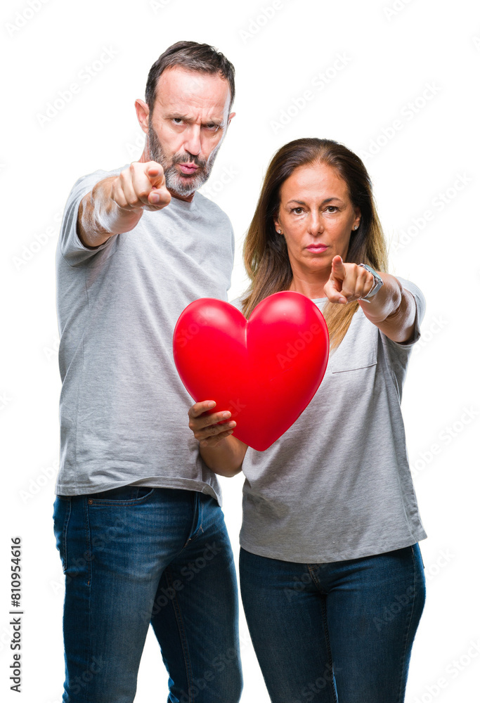 Middle age hispanic casual couple in love holding red heart over isolated background pointing with finger to the camera and to you, hand sign, positive and confident gesture from the front Middle age hispanic casual couple in love holding red heart over isolated background pointing with finger to the camera and to you, hand sign, positive and confident gesture from the front