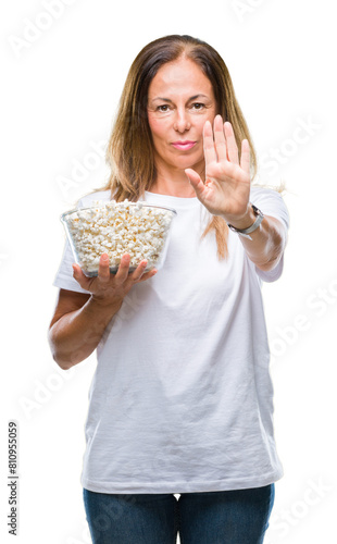 Middle age hispanic woman eating popcorn over isolated background with open hand doing stop sign with serious and confident expression, defense gesture