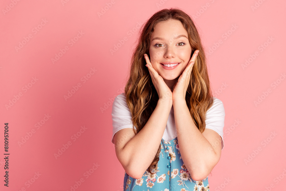 Photo of cute young girl hands touch cheeks empty space wear dress isolated on pink color background Photo of cute young girl hands touch cheeks empty space wear dress isolated on pink color background