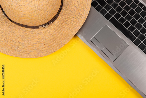 Laptop and straw hat on yellow background. Work at holiday. Concept of travelling on summer vacation. Business trip to the south. Freelancer's job. Working weekend. Visiting card with empty space