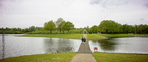 Wooden walk bridge leading to island wide angle panorama landscape of recreational pond Lageveld in Wierden with picnic field and leisure area photo