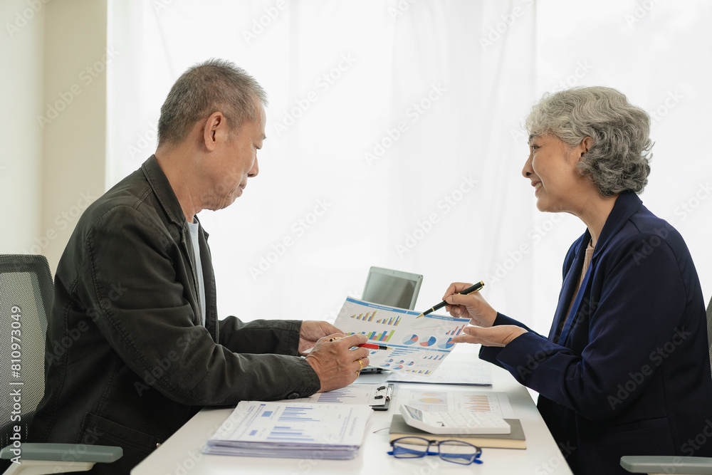 Two senior Asian businessmen analyze finances with documents. Man and woman work on financial documents to analyze and calculate. Look happy at work. Two senior Asian businessmen analyze finances with documents. Man and woman work on financial documents to analyze and calculate. Look happy at work.