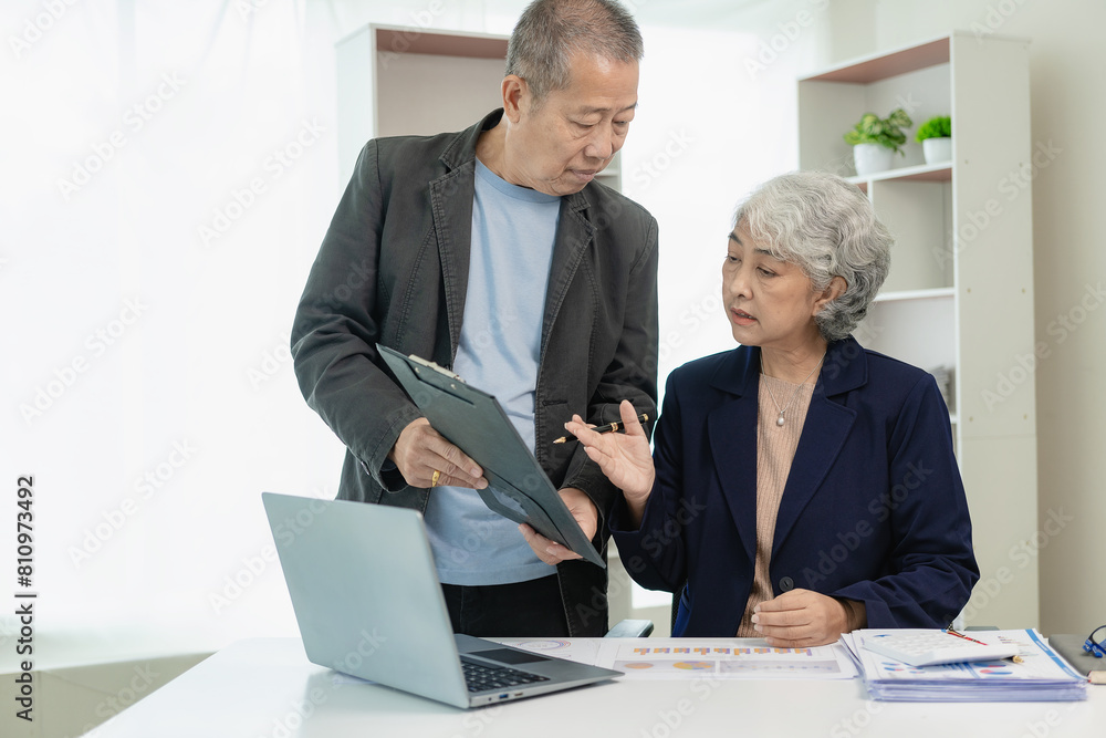Two senior Asian businessmen analyze finances with documents. Man and woman work on financial documents to analyze and calculate. Look happy at work. Two senior Asian businessmen analyze finances with documents. Man and woman work on financial documents to analyze and calculate. Look happy at work.