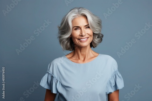 Portrait of beautiful happy 55s old tanned woman with long bob haircut in light blue blouse on blue background photo