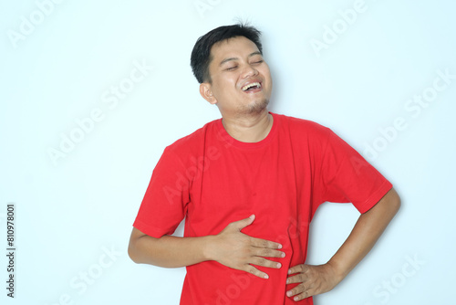 Young Asian man touching his belly with relieved expression. Wearing red a shirt photo