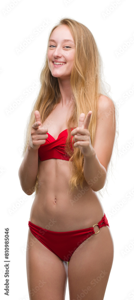 Blonde teenager woman wearing red bikini pointing fingers to camera with happy and funny face. Good energy and vibes. Blonde teenager woman wearing red bikini pointing fingers to camera with happy and funny face. Good energy and vibes.