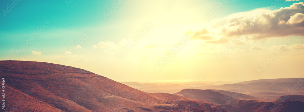 Mountainous desert with colorful cloudy sky. Judean desert in Israel at sunset. Horizontal banner