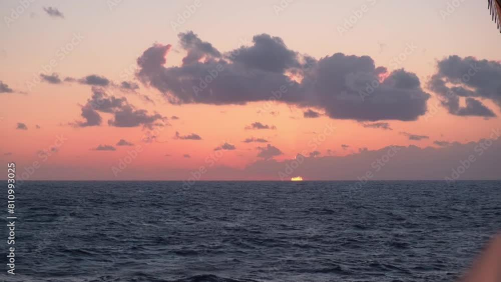 Pink ocean sunset with picturesque clouds, golden disk of sun peeks through haze above horizon Pink ocean sunset with picturesque clouds, golden disk of sun peeks through haze above horizon