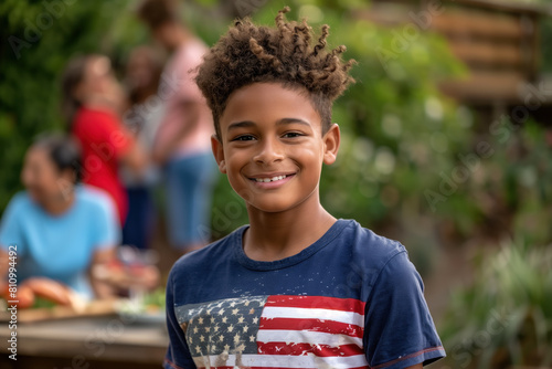 A happy young man wearing an American flag t-shirt smiles during a family picnic in the backyard. Independence Day Celebration.