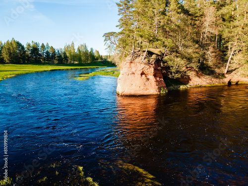 vibrant river landscape with red cliffs and lush greenery under a clear blue sky