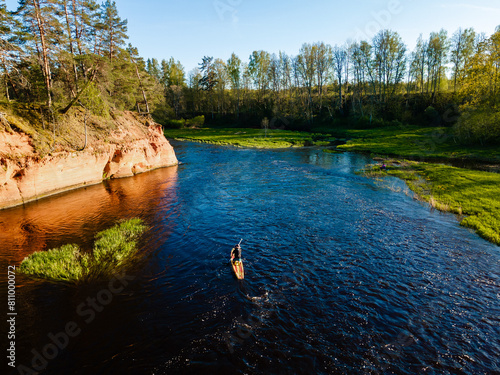 paddle boarder exploring a scenic river with red cliffs and lush greenery during sunset