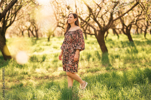 Outdoors portrait of a smiling woman wearing dress walking in almond orchard.