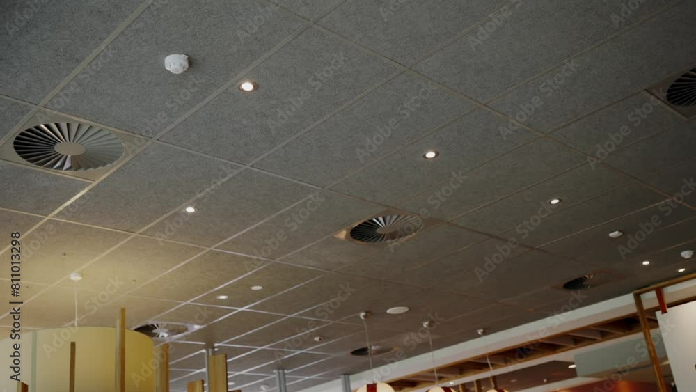 Interior image showing a detailed view of a modern ceiling with integrated lighting fixtures and acoustic panels in a public building. Modern Ceiling Design in a Public Space with Lighting Interior image showing a detailed view of a modern ceiling with integrated lighting fixtures and acoustic panels in a public building. Modern Ceiling Design in a Public Space with Lighting