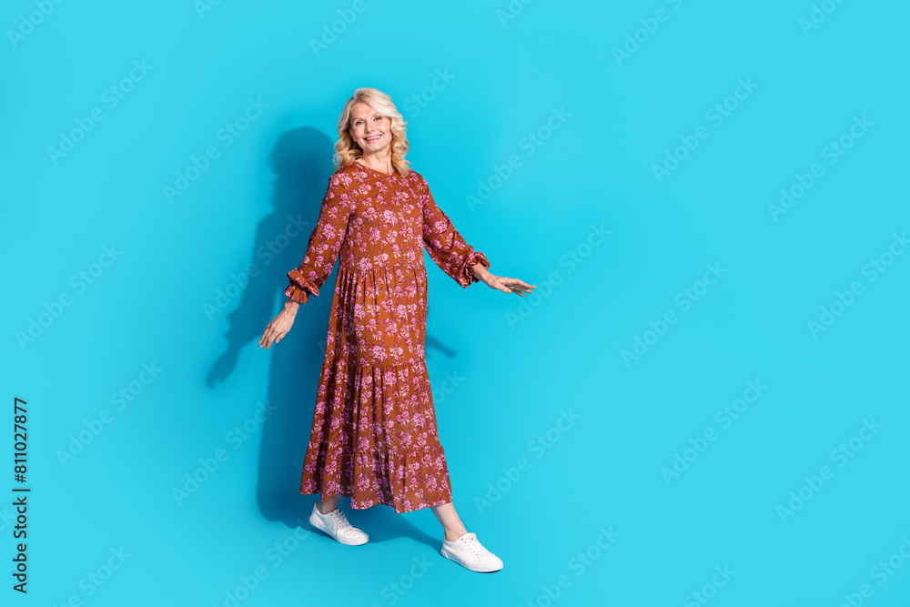 Full length photo of shiny attractive lady dressed brown clothes smiling walking empty space isolated blue color background Full length photo of shiny attractive lady dressed brown clothes smiling walking empty space isolated blue color background