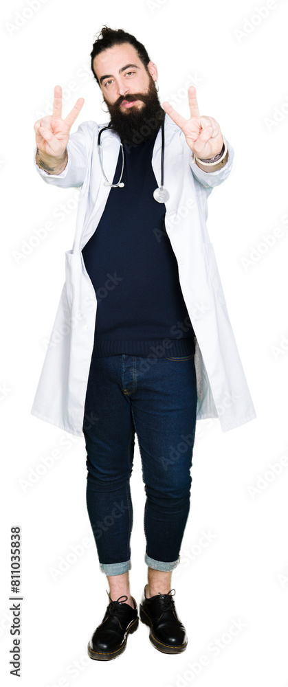 Doctor with long hair wearing medical coat and stethoscope smiling looking to the camera showing fingers doing victory sign. Number two. Doctor with long hair wearing medical coat and stethoscope smiling looking to the camera showing fingers doing victory sign. Number two.