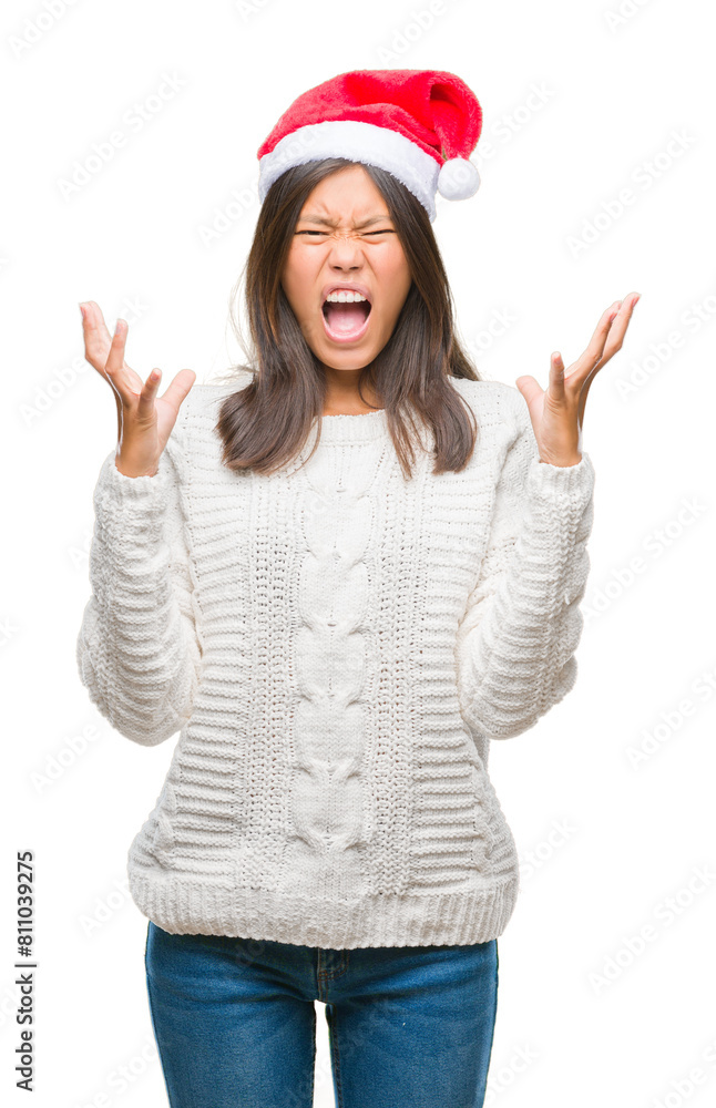 Young asian woman wearing christmas hat over isolated background crazy and mad shouting and yelling with aggressive expression and arms raised. Frustration concept.