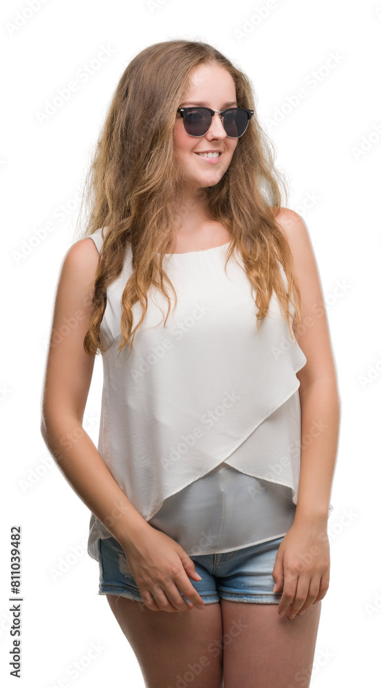 Young blonde woman wearing sunglasses looking away to side with smile on face, natural expression. Laughing confident.