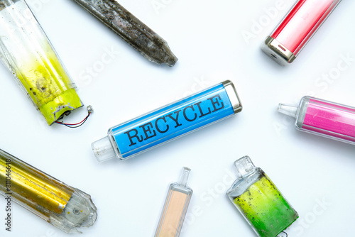 Discarded electronic cigarette vapes, one labelled: RECYCLE. Shot isolated on white paper