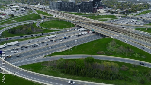 Aerial view over highway expanse, commuter cars threading through city's vascular roadways. Drone panorama over city highways, vehicles in synchronized movement, epitome of urban connectivity.