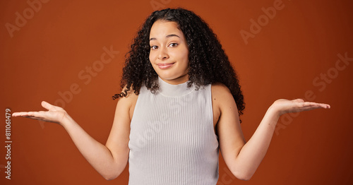 Portrait, woman and studio with comparison, choice and hand gesture on background with shrugging shoulders. Female person, options and doubt on backdrop in mockup space in indecision for alternatives