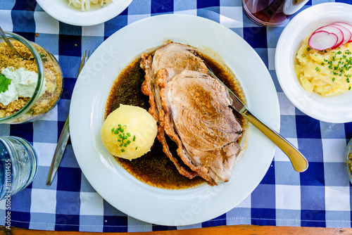 Traditioneller bayerischer Schweinebraten mit Knödel und Sauerkraut auf blau-weiß kariertem Tischtuch