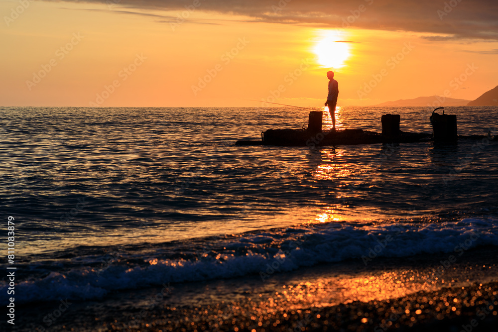 the silhouette of a fisherman against the background of a sunset at sea