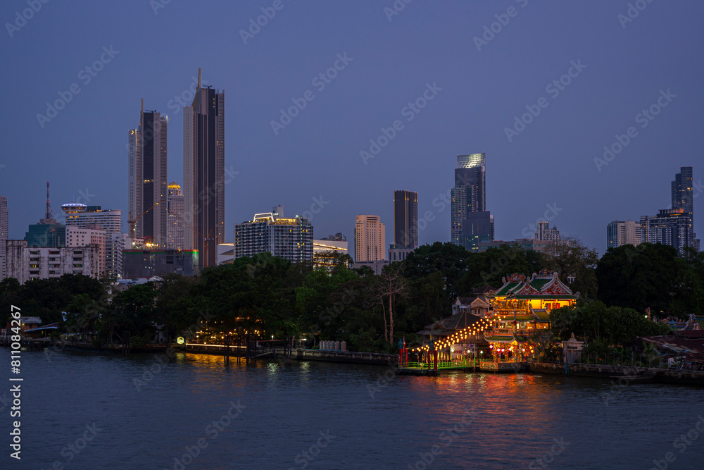 Fototapeta premium Urban cityscape with skyscrapers and Guan Yu Shrine (Khlong San) by the Chao Phraya River in Bangkok, Thailand at dusk.