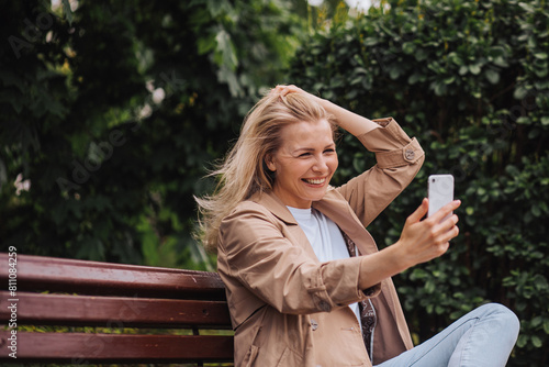 Closeup portrait of smiling cheerful young woman taking selfie while relaxing in city park