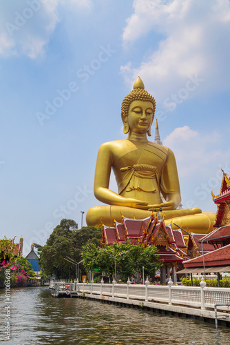 Big, tall and golden Buddha statue at the Wat Paknam (Pak Nam) Phasi Charoen Temple by a canal (khlong) in Bangkok, Thailand on a sunny day. It's a major religious landmark and attraction in the city.