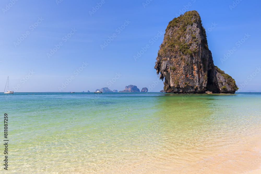 Stunning landscape of a tall limestone cliff, blue sky and turquoise sea at the Phranang (Phra Nang) Beach in Railay, Krabi, Thailand on a sunny day.
