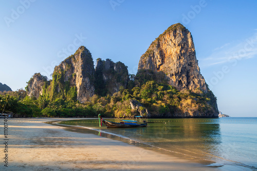 Scenic view of a long-tail boat at the empty Railay West beach and high limestone cliffs in Railay, Krabi, Thailand, on a sunny morning. © tuomaslehtinen