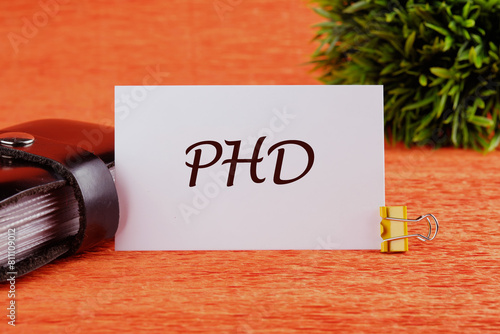 Word PhD. Doctor of Philosophy. PHD on a white card in front of an orange background with a plant in the background photo