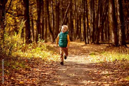 Little boy running in the autumn forest. Happy child having fun outdoors.