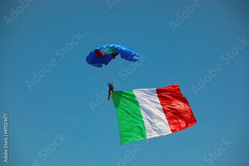 paratrooper with huge Italian flag on blue sky during National Alpini rally of Italian Military Corp photo