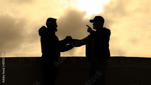 silhouette of two men shaking hands yellow sky